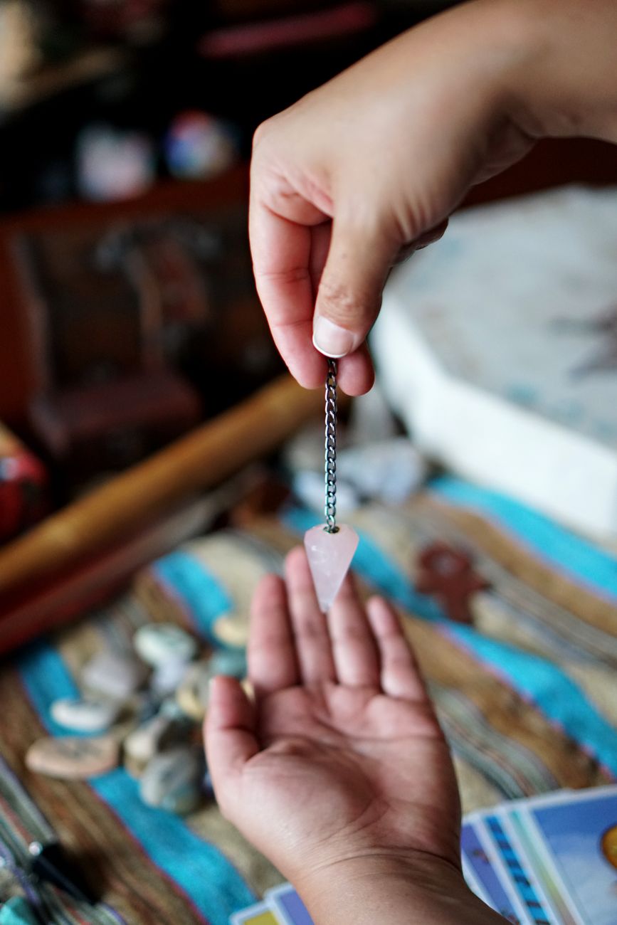 hands holding rose quartz pendulum in spiritual setting