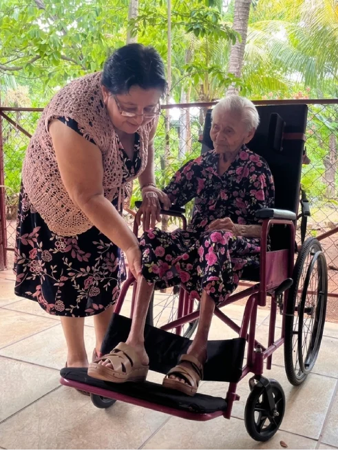 Rosalina Flores atiende con afecto a una adulta mayor en silla de ruedas dentro de las instalaciones de casa hogar de adultos mayores en Juigalpa, Nicaragua.